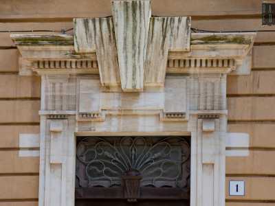 ...con una trabeazione di stampo neoclassico con triglifi e cornice a dentelli spezzata da un massiccio elemento centrale